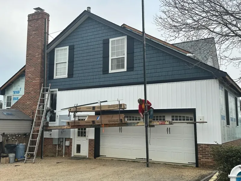 Summit Exteriors installer on staging boards mid-siding installation with new navy and white vertical siding in Prince Frederick, MD