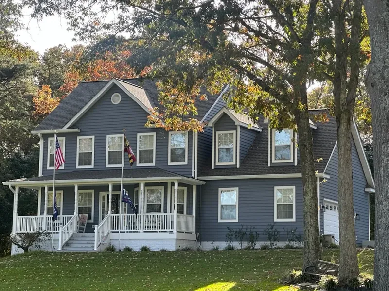 Two-story colonial with new dark blue vinyl siding, white trim, and wraparound porch in Hollywood, MD